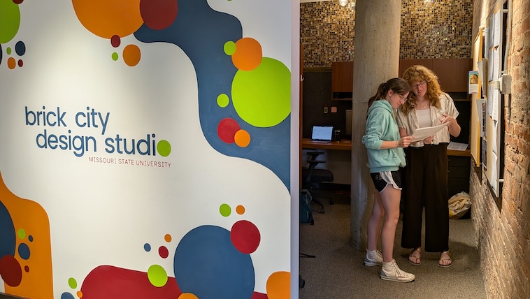 Two student graphic designers confer next to entrance of BCDS