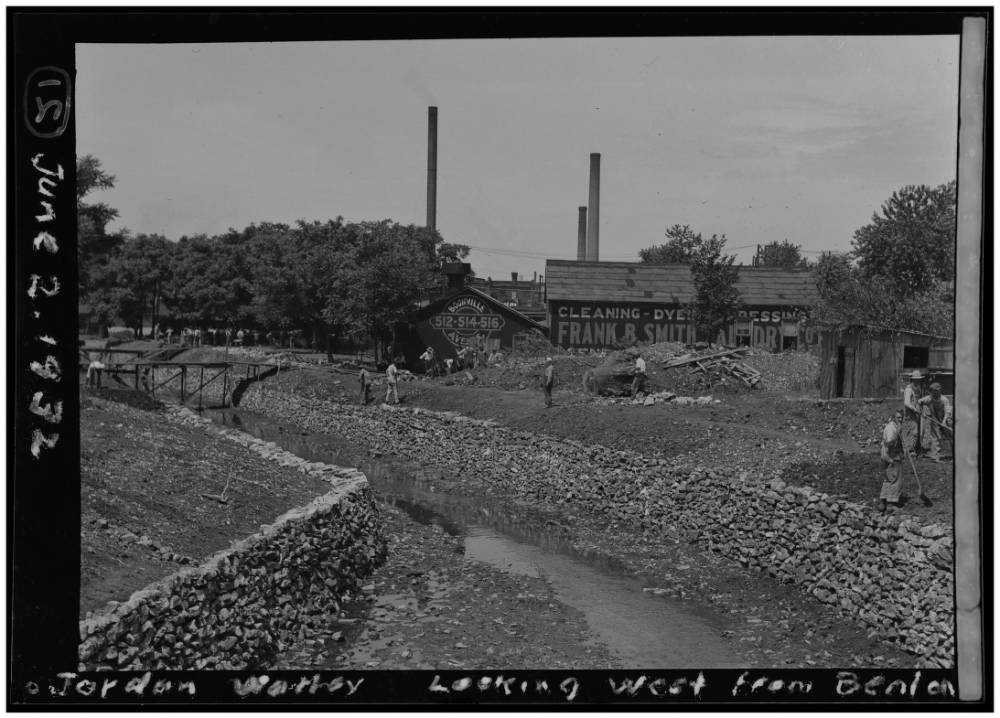 greyscale photo of creek and back of buildings